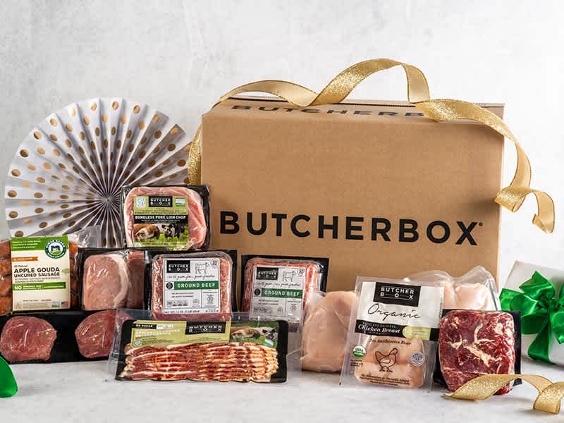 A wide selection of meat, seafood, and poultry on a white surface with a ButcherBox box and ribbons