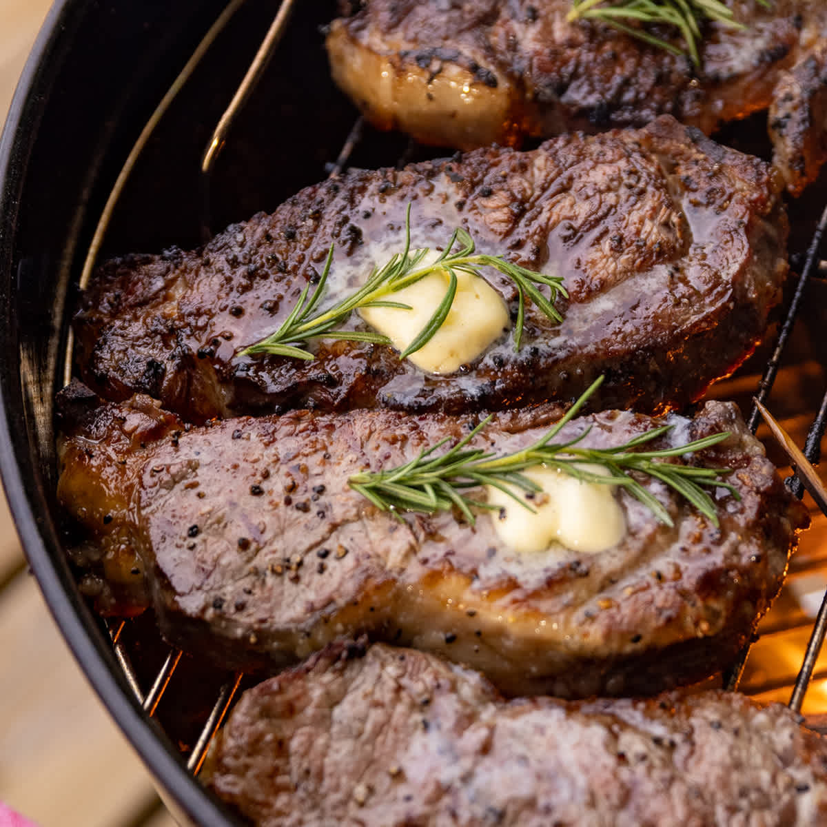 Steaks cooking on the grill with melting rosemary butter